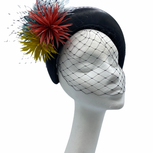 Black leather crown finished with mint/coral/yellow flower detail. Black veiling covers the face entirely.
