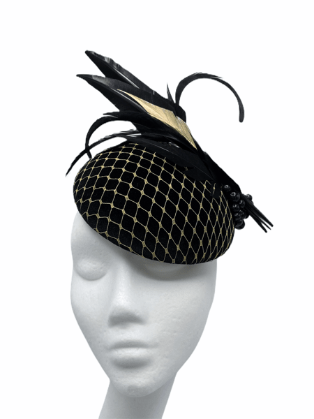 Black velvet pillbox with gold netting overlay, finished with black and gold arrow feathers.