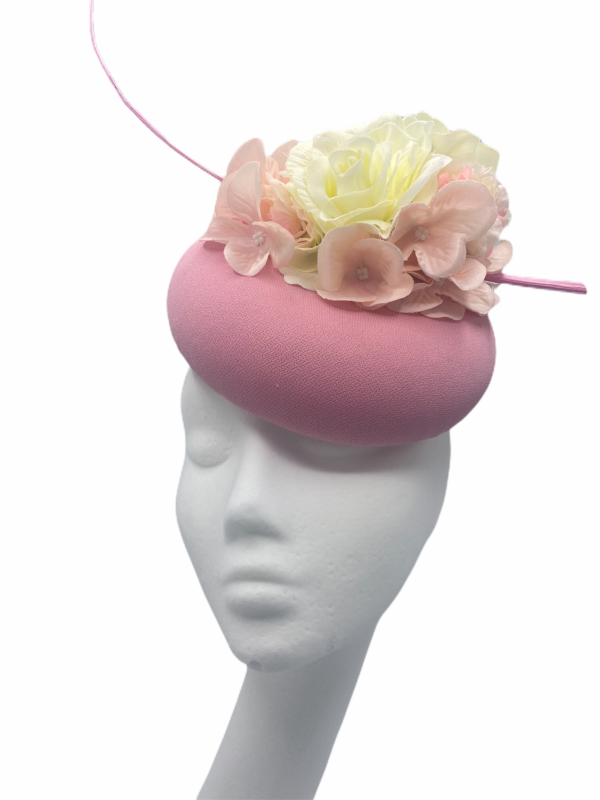 Baby pink pillbox with baby pink and white flowers to the top with a pink quill.