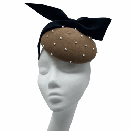 Taupe felt based headpiece encrusted in pearls with black felt bow detail .