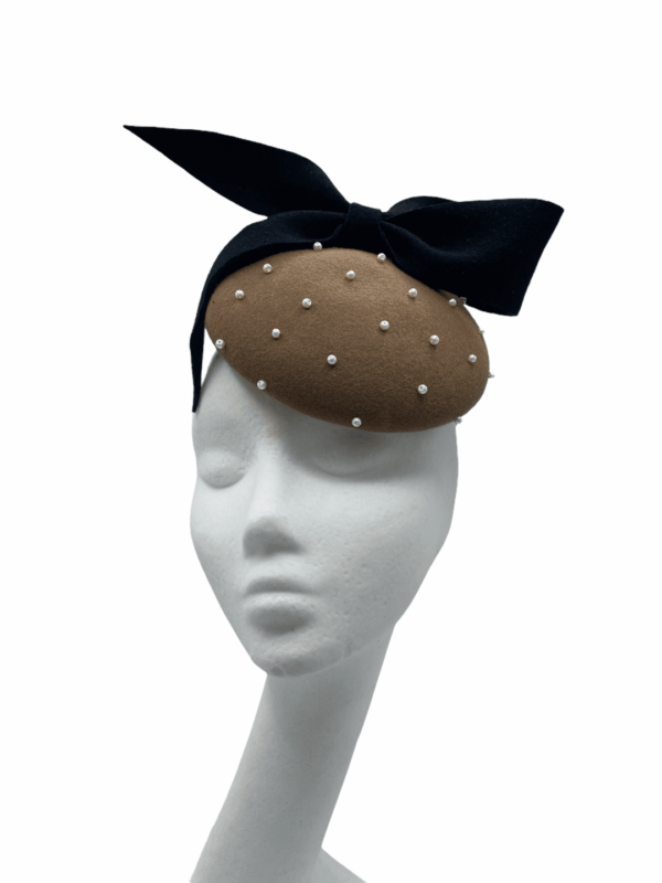 Taupe felt based headpiece encrusted in pearls with black felt bow detail .