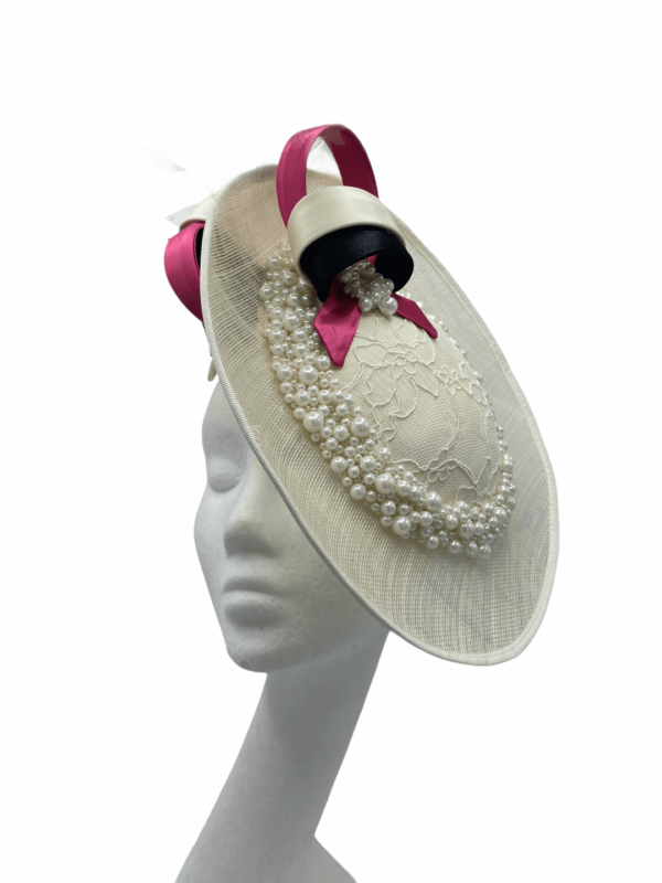 Ivory/cream side saucer disc headpiece, cream/black/pink satin swirl detail to the top finished with spray of ivory feather detail. Ivory headband with ivory circular lace detail to the side surrounded with pearls.