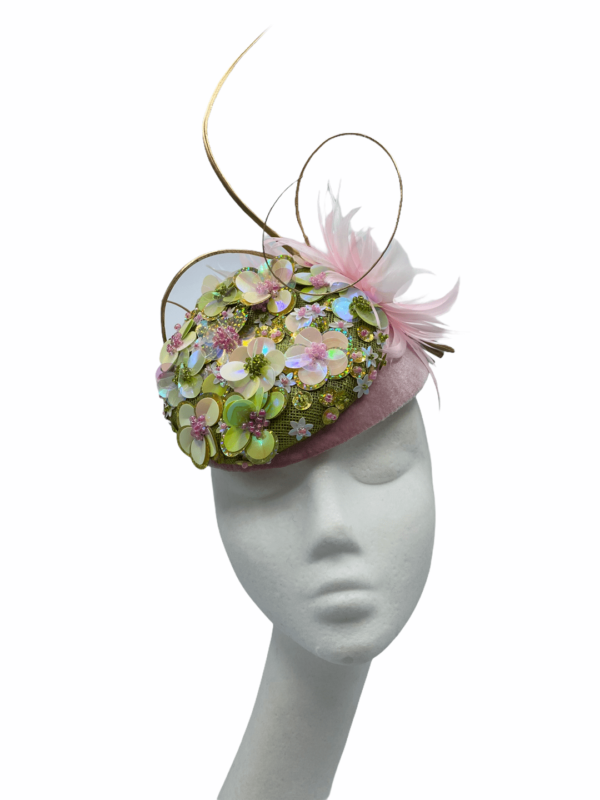 Pink velvet base headpiece with green foil flower detail and finished with gold quills .