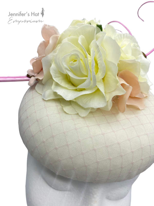 Cream pillbox base with a pink netting overlay to base. Pink/cream flowers to the top finished with a baby pink quills.