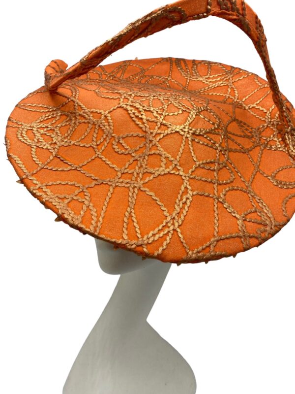 Orange saucer hat with large swirl detail with gold design detail overlay. 