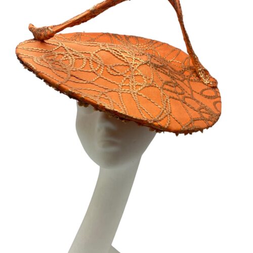 Orange saucer hat with large swirl detail with gold design detail overlay. 