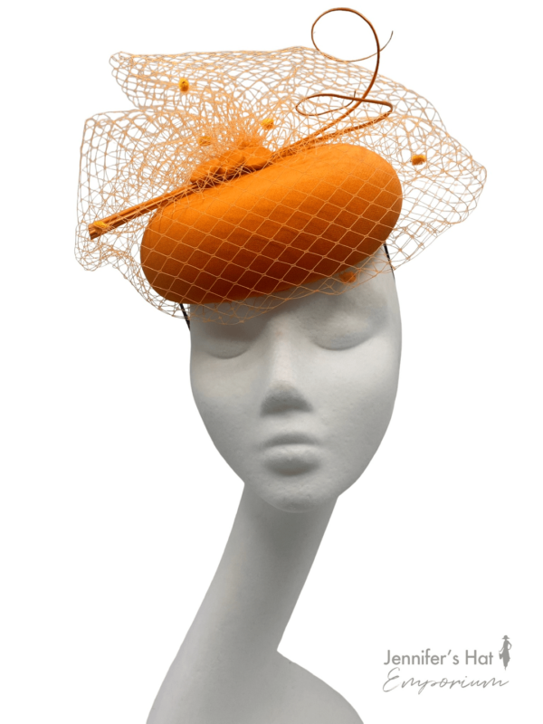Orange pillbox headpiece finished with matching orange veiling and orange quill detail.