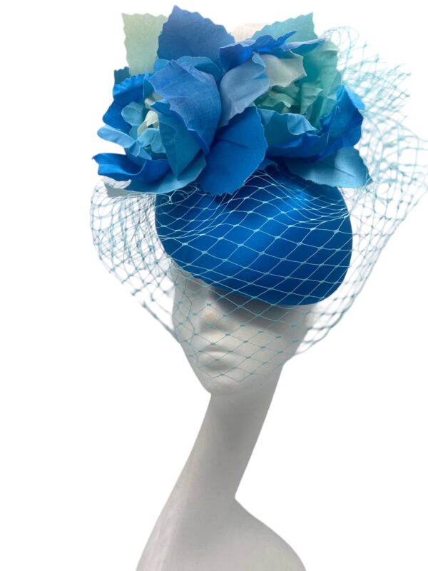 Large turquoise and blue headpiece with an array of handmade flowers and finished with veiling that partly covers the face.